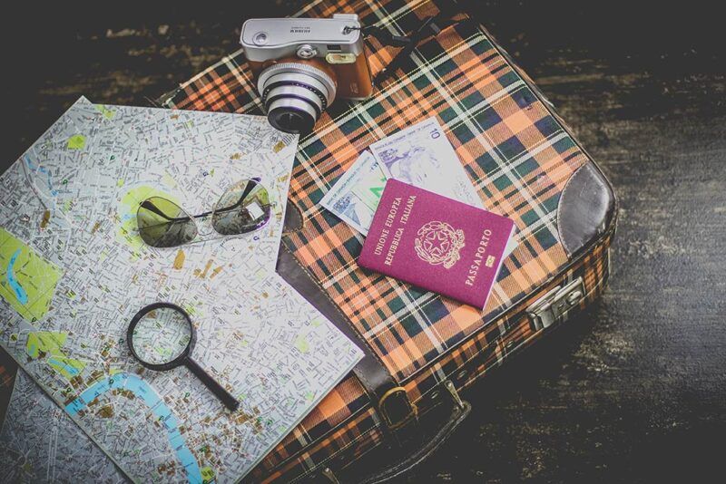 maleta con mapas, maquina de fotos, pasaporte y gafas de sol apoyados encima - weroad