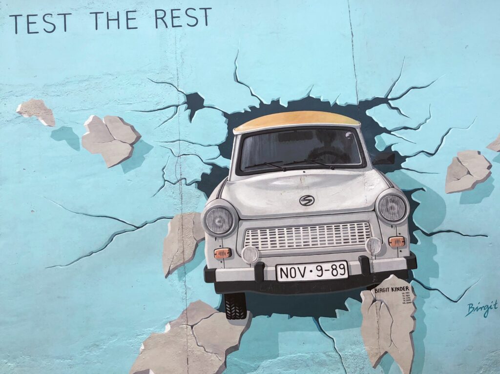 Porzione del Muro di Berlino in cui è raffigurata una Trabant grigia, auto simbolo della Germania Est, che lo sfonda.