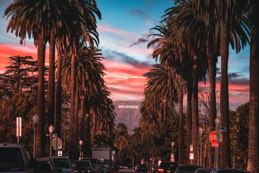 La Hollywood Sign svetta in lontananza immersa in una cornice di palme e automobili al tramonto