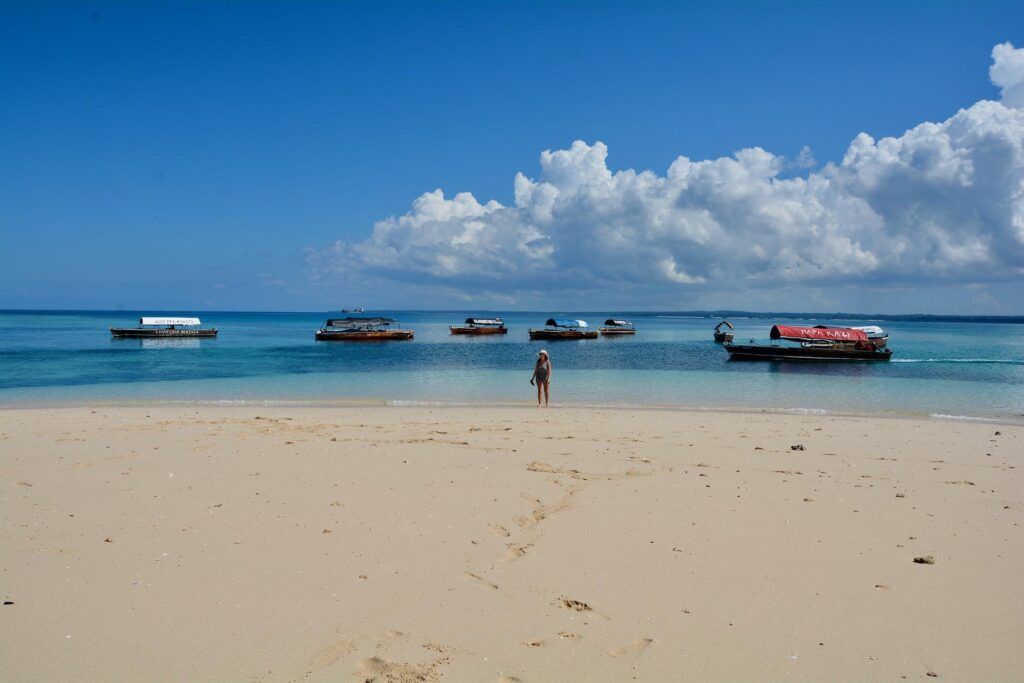 Una donna cammina lungo la spiaggia di Nakupenda con delle barche sullo sfondo