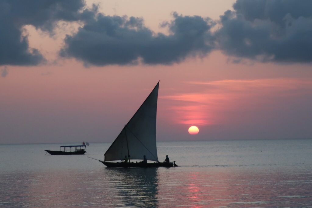 Una barca a vela solca il mare calmo di Nungwi beach al tramonto