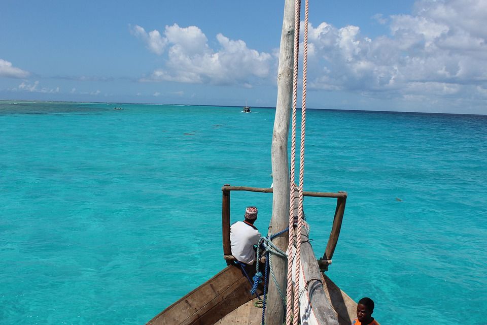 Un uomo con un cappello tipico siede sulla prua di un'imbarcazione che solca un mare cristallino