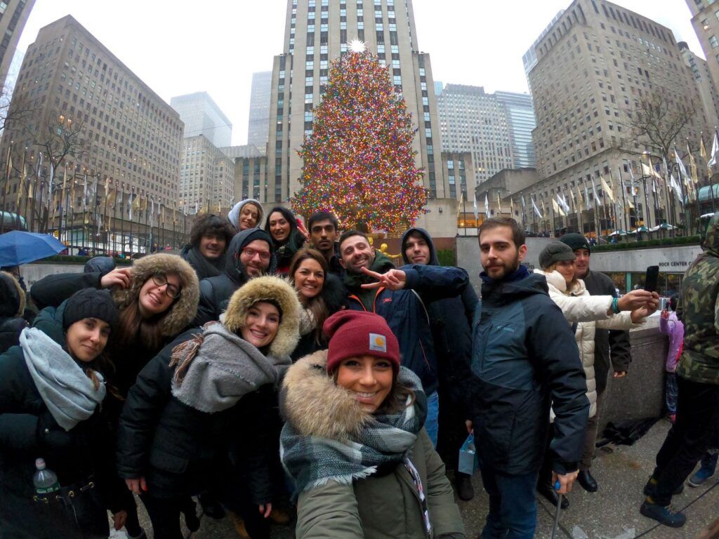 un gruppo di persone sorride davanti all'albero di Natale del Rockefeller Center durante il ponte dell'Immacolata