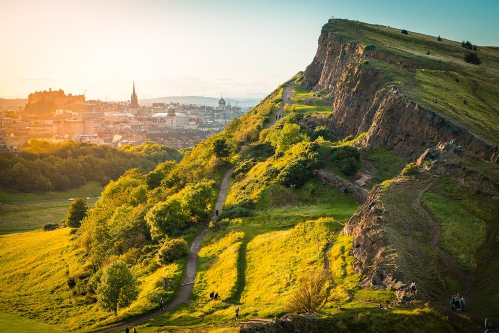 Dalla roccia coperta di vegetazione di Arthur's Seat si intravede la città di Edimburgo al tramonto