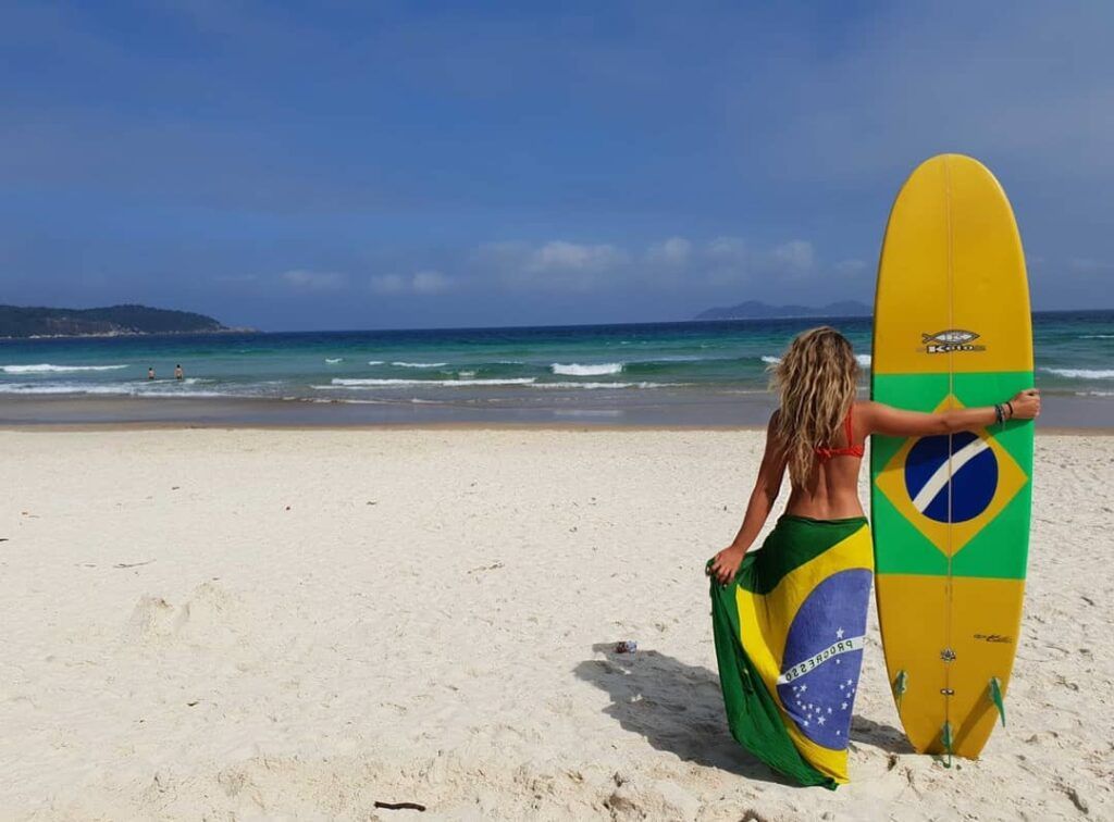 Una ragazza bionda con tavola da surf e pareo con la bandiera del Brasile