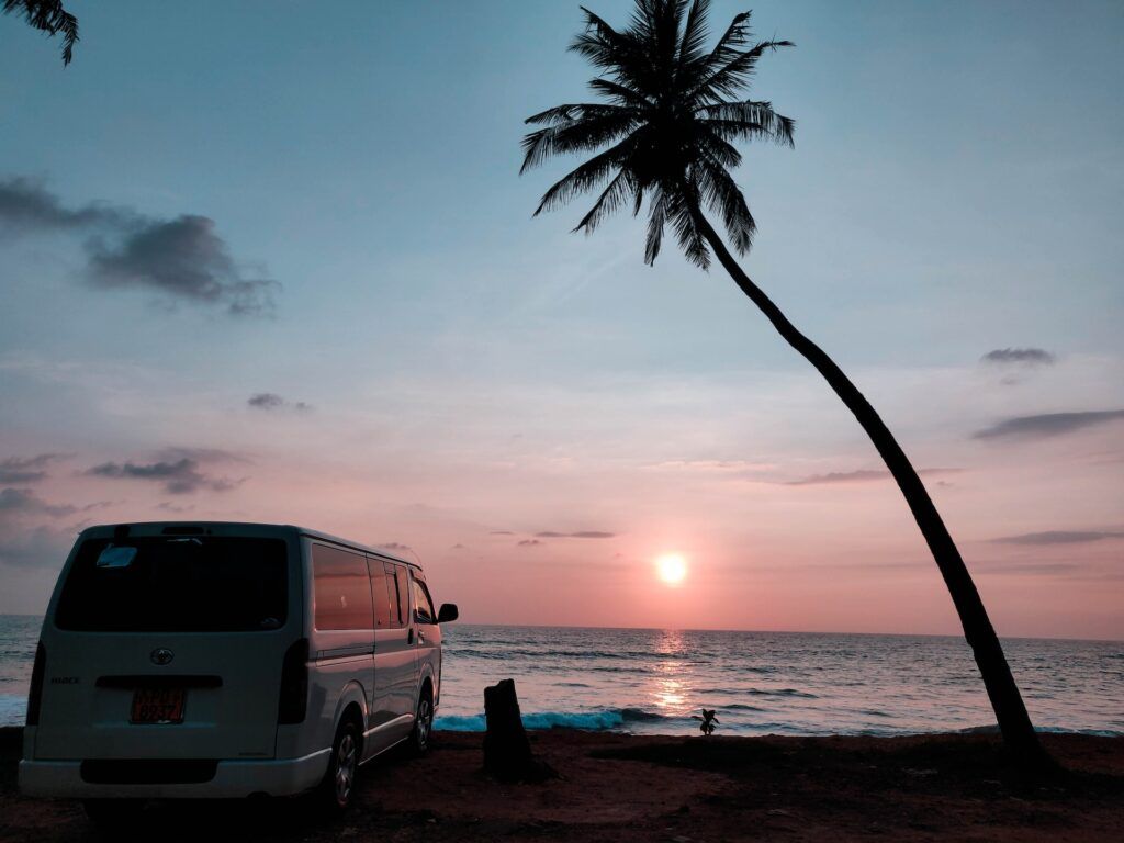Un van vicino alla spiaggia con una palma al tramonto