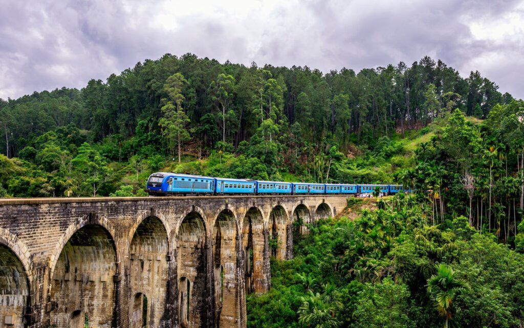 Treno blu circondato da alberi su un ponte a nove archi in Sri Lanka
