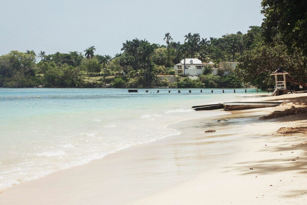 Spiaggia di sabbia bianca e mare cristallino con palme e una casa bianca