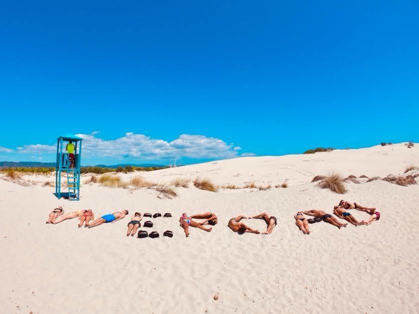 Foto di un gruppo di WeRoaders che sdraiati nella sabbia creano la scritta WeRoad
