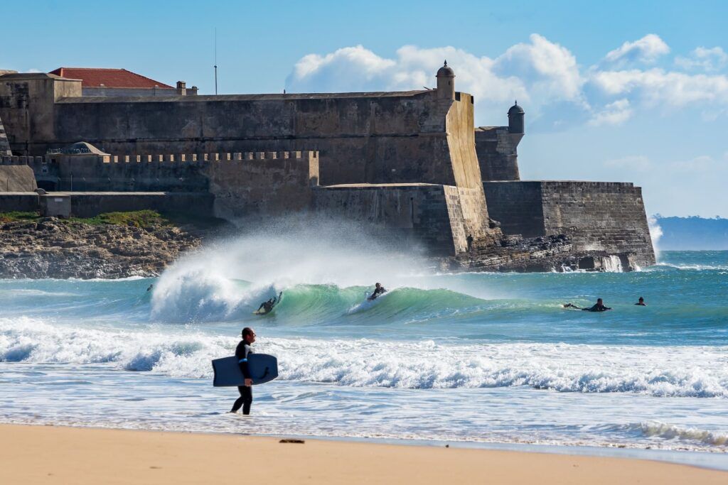 Un edificio storico si affaccia sul mare solcato da persone che fanno surf