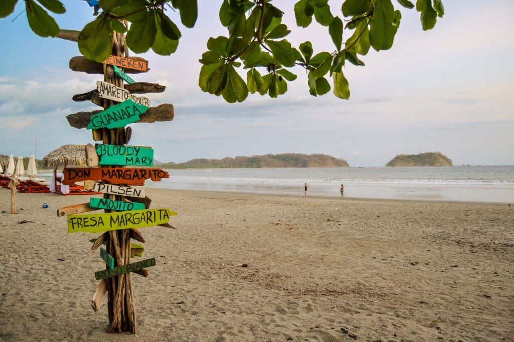 Un palo con dei cartelli affisso in spiaggia in Costa Rica al tramonto