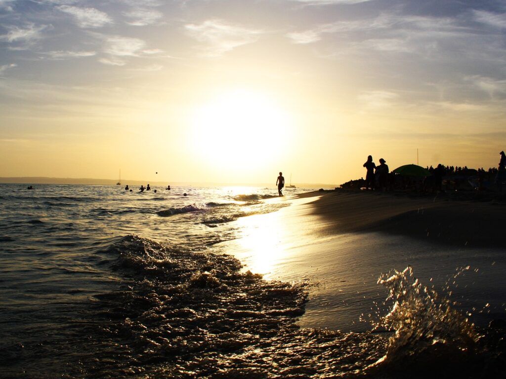 Delle persone camminano lungo Playa es Pujols al tramonto