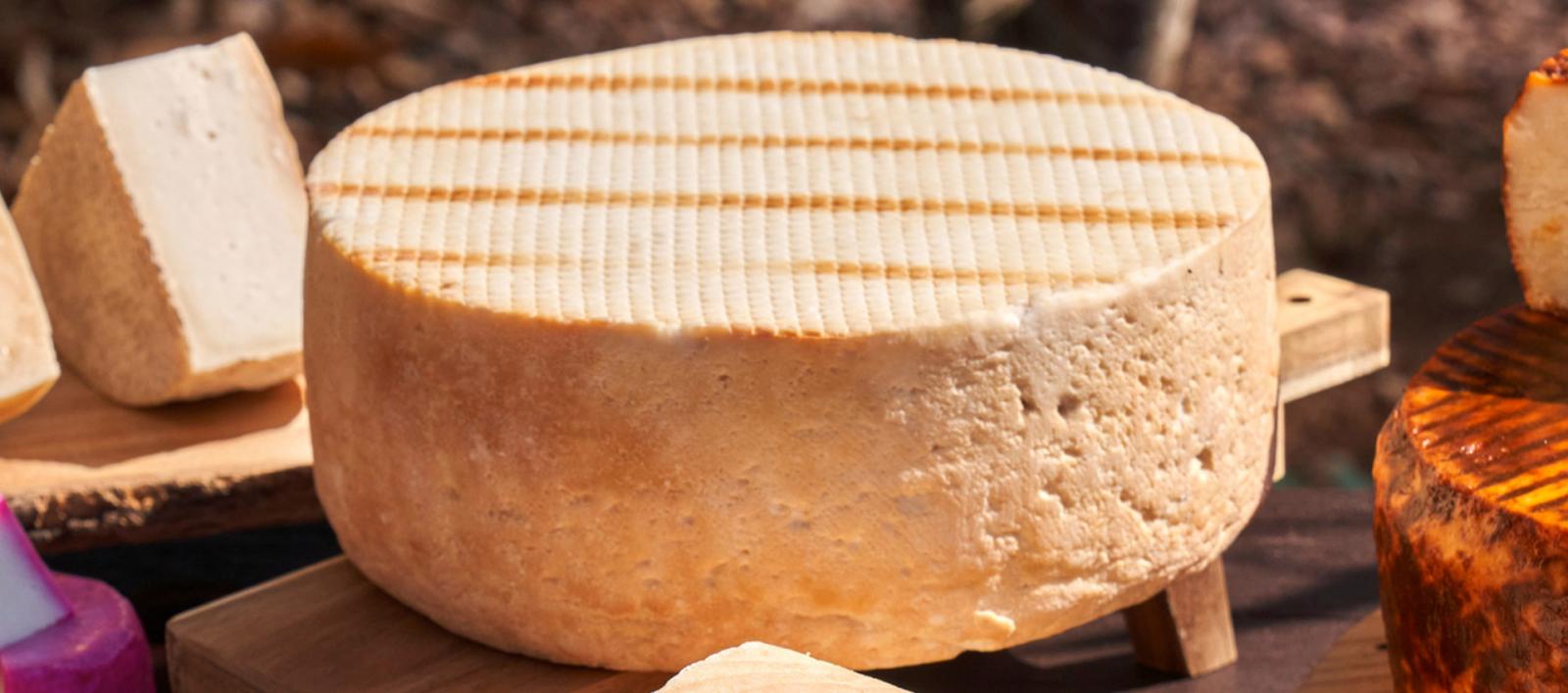 Una forma intera di formaggio canario posizionata su un tagliere di legno, circondata da altri pezzi di formaggio
