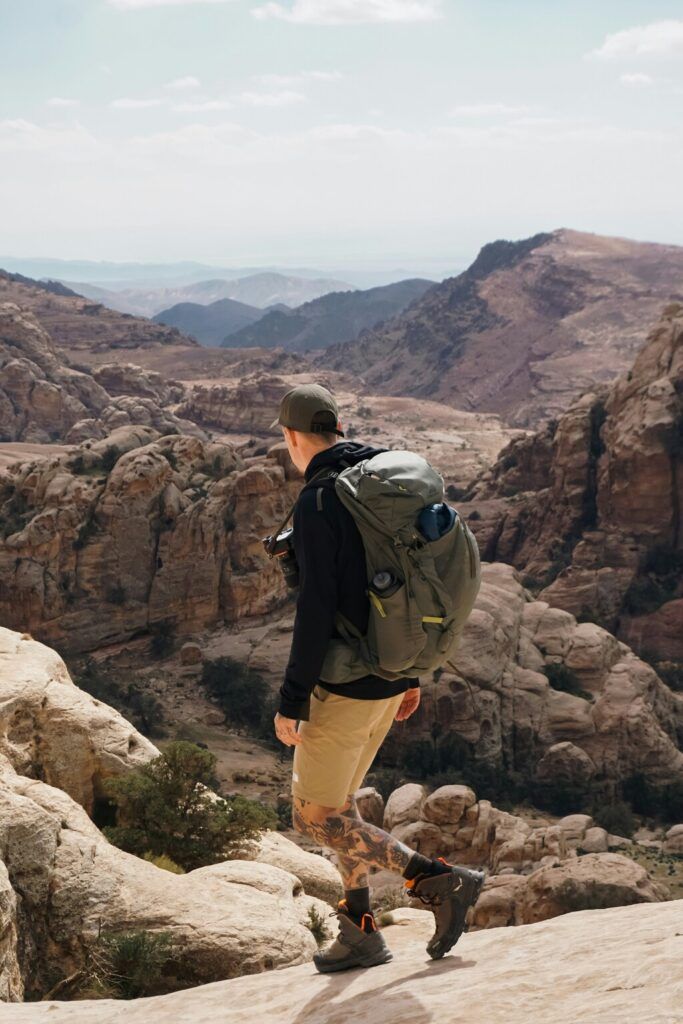 Una persona, con un grande zaino e abbigliamento da trekking, osserva il paesaggio aspro e maestoso di Petra, in Giordania.