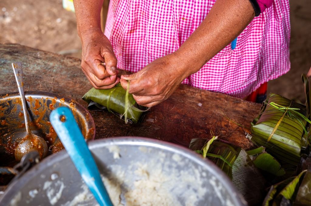 Preparazione artigianale dei tamales colombiani: mani esperte avvolgono l’impasto di mais in foglie di banano, secondo una tradizione che profuma di casa.