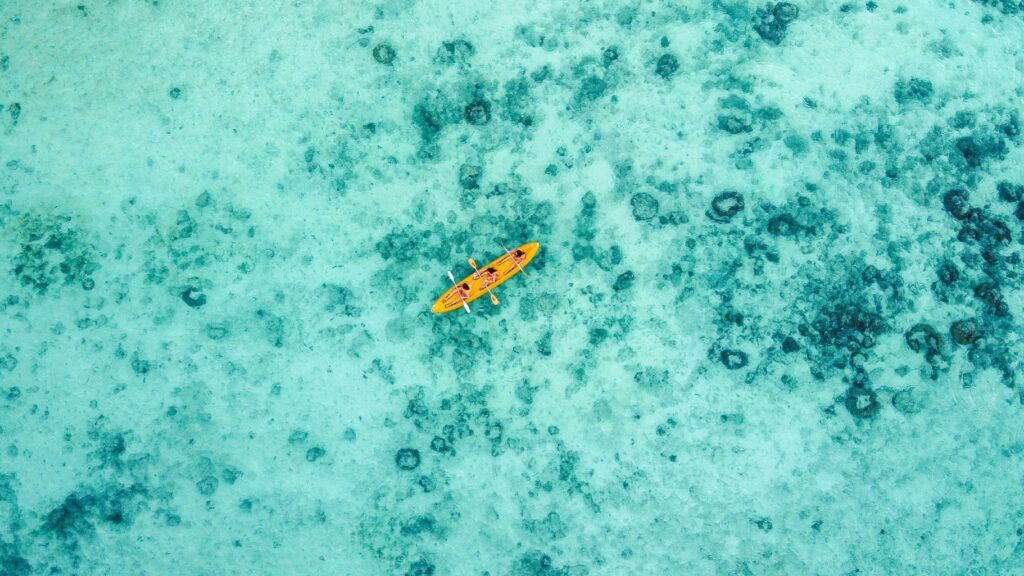Kayak arancione su acque turchesi e fondale corallino vista dall’alto: viaggiare tra le isole