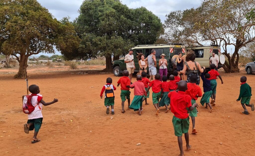 Un gruppo di bambini in uniforme scolastica corre verso un gruppo di viaggiatori WeRoad nella savana africana.