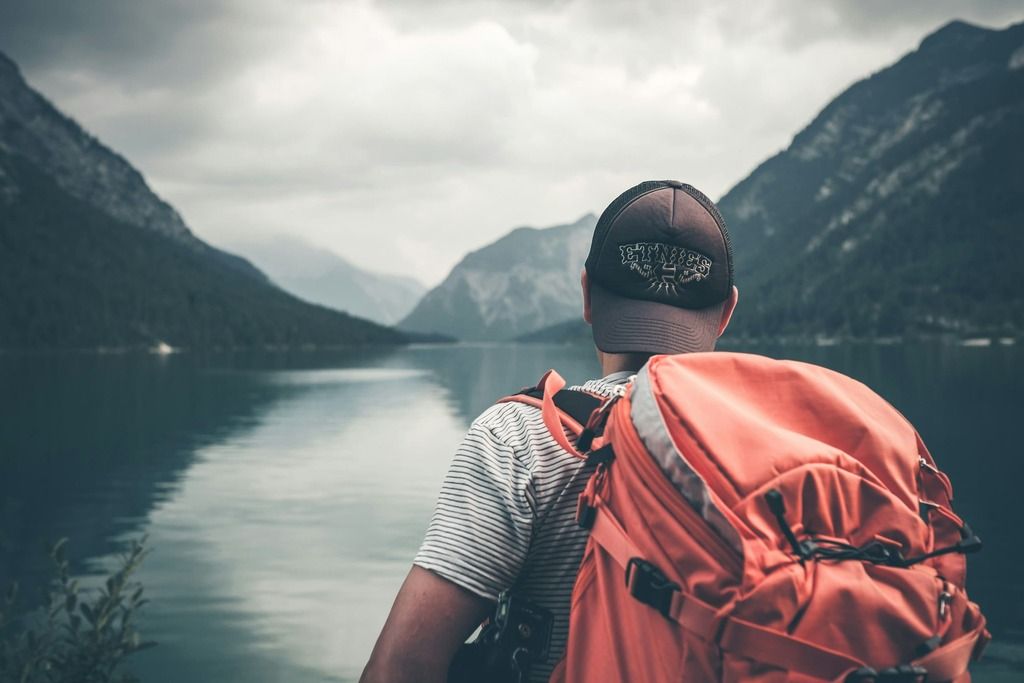 Ragazzo viaggiatore ammira un lago tra le montagne.
