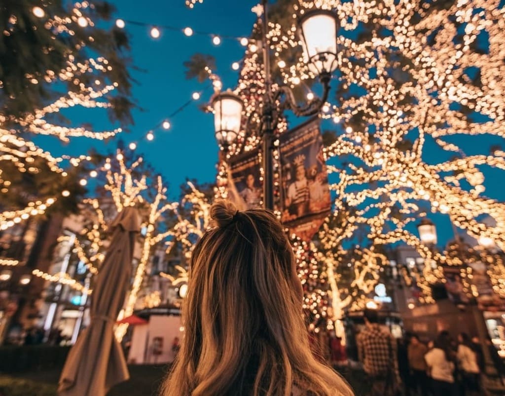 Donna di spalle osserva un viale addobbato con luci natalizie e decorazioni festive, atmosfera magica dei mercatini di Natale italiani.